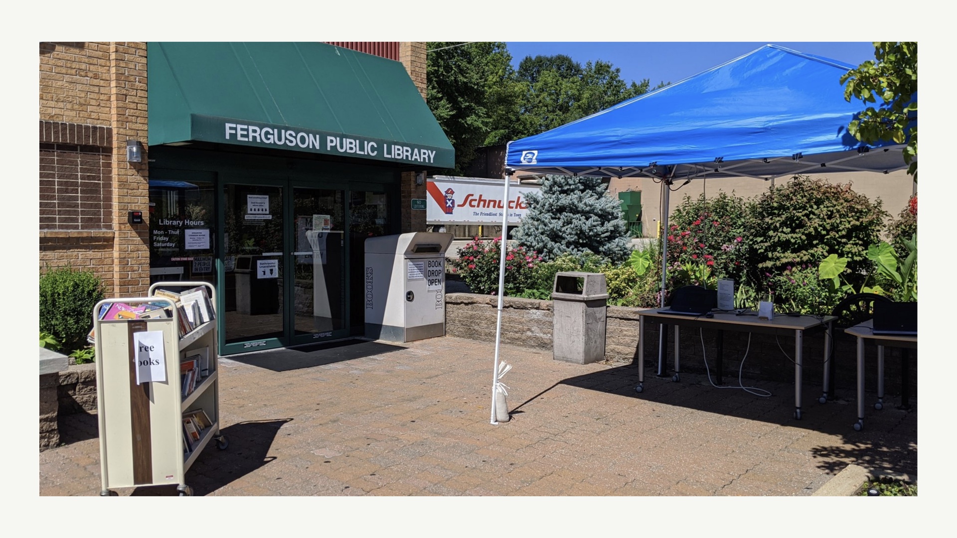 [photograph of Ferguson Public Library with their copiers and some laptops moved outside along with book cart offering free books]