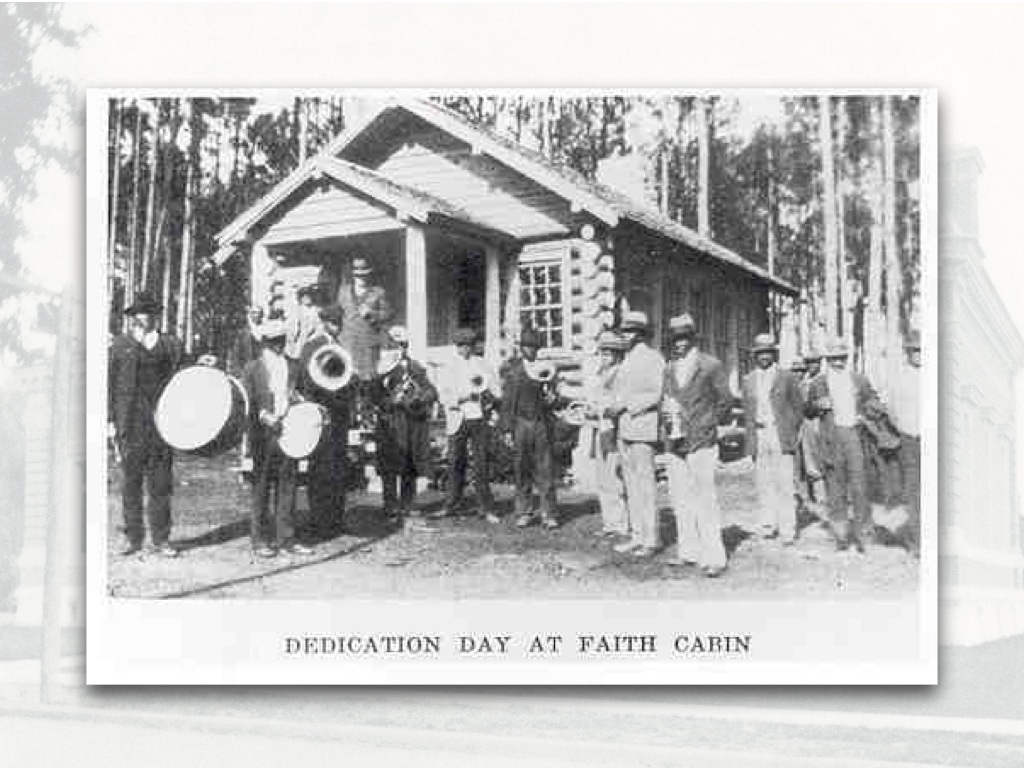 Very old-timey image of a group of young black men in nice outfits with instruments standing in front of a log cabin with the caption 