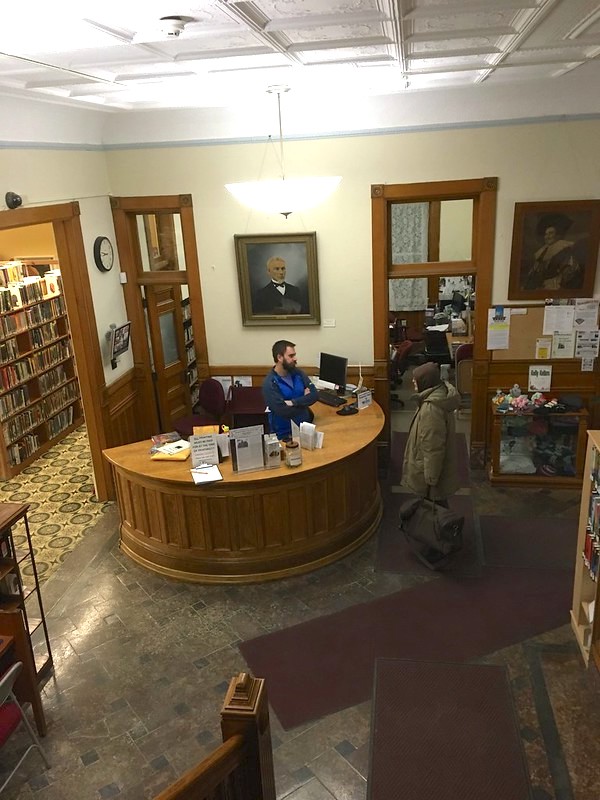 a view of the library from the top of the stairs showing a gorgeous circular reference desk with a librarian talking with a patron