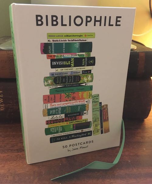 the cover of a box of postcards that is called BIBLIOPHILE and the postcard on the cover is a stack of books
