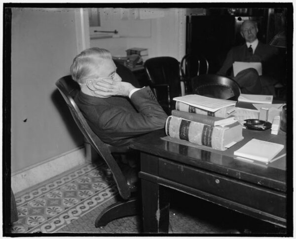 an older white man sits at a table behind a pile of books