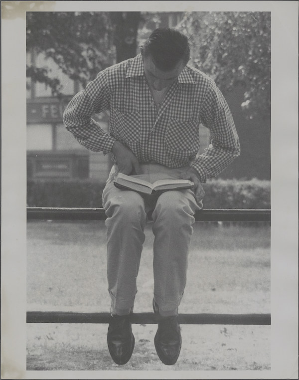 a man sitting outside on a bench or wall looking down at a book that is open in his lap.