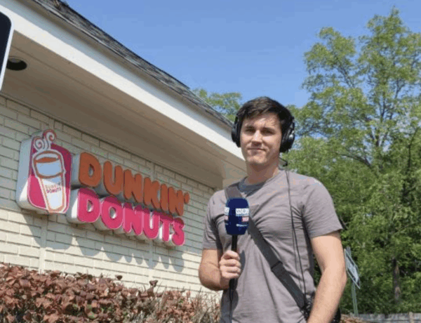 Matt Shearer, a radio host, standing in front of a Dunkin Donuts wearing his radio gear and holding a microphone.