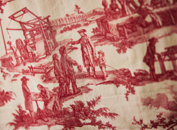 photograph of some fabric showing people working with old time machines outdoors.